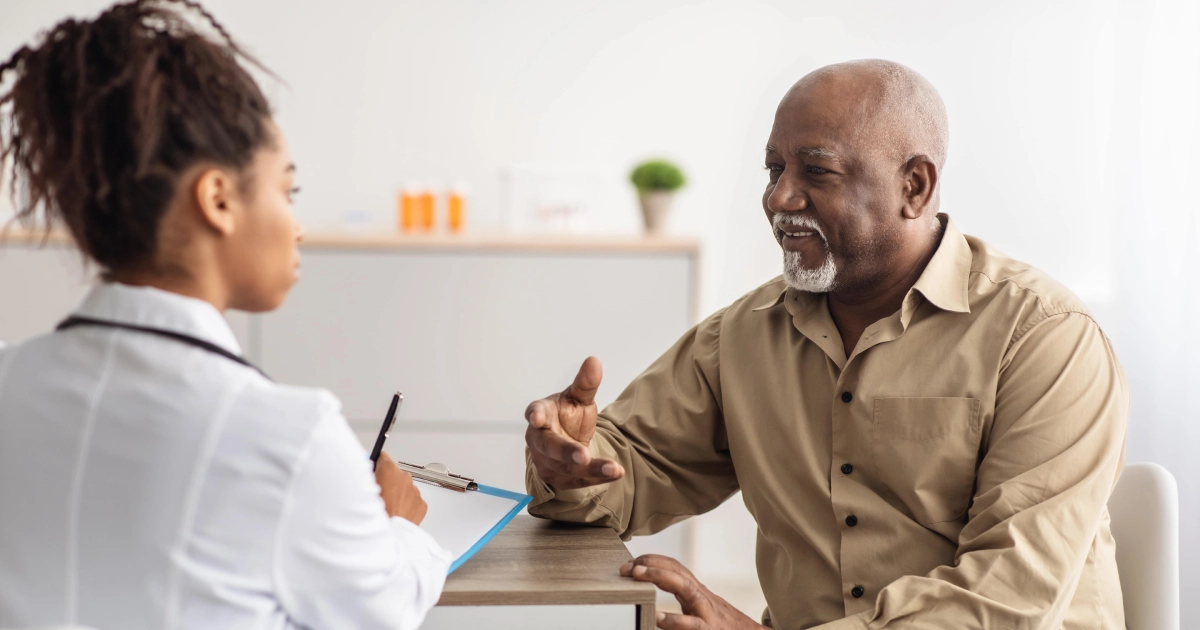 A smiling senior man is gesturing while consulting with a female doctor or healthcare provider at a Medspa in Cedar Park, TX, who is taking notes in a modern clinic.